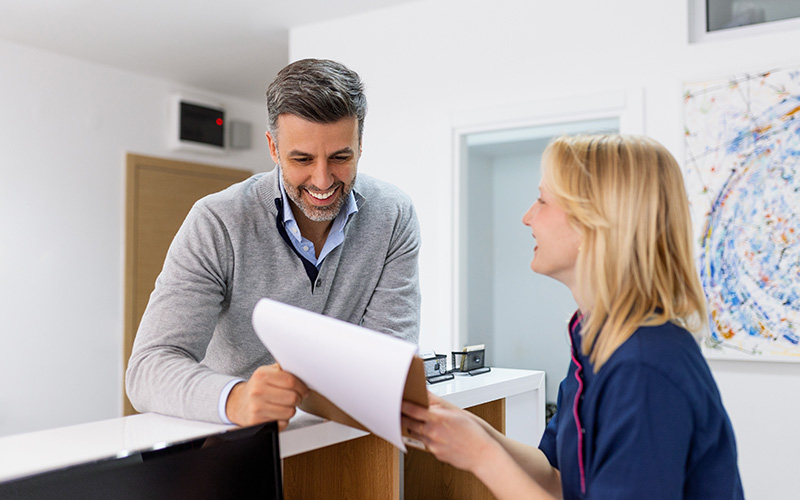 A man and a woman in a professional setting, with the man handing over papers to the woman.